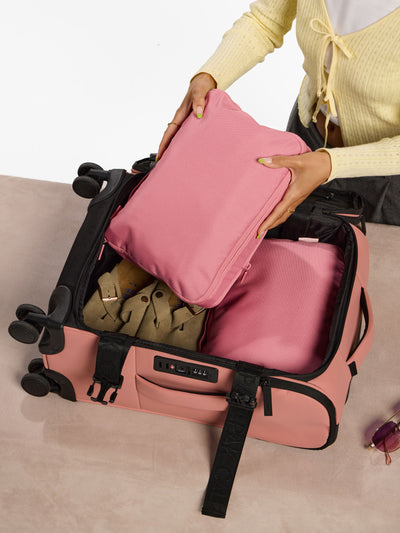 Model placing pink tea rose CALPAK Medium Compression Packing Cubes within Luka Soft-Sided Carry-On Luggage