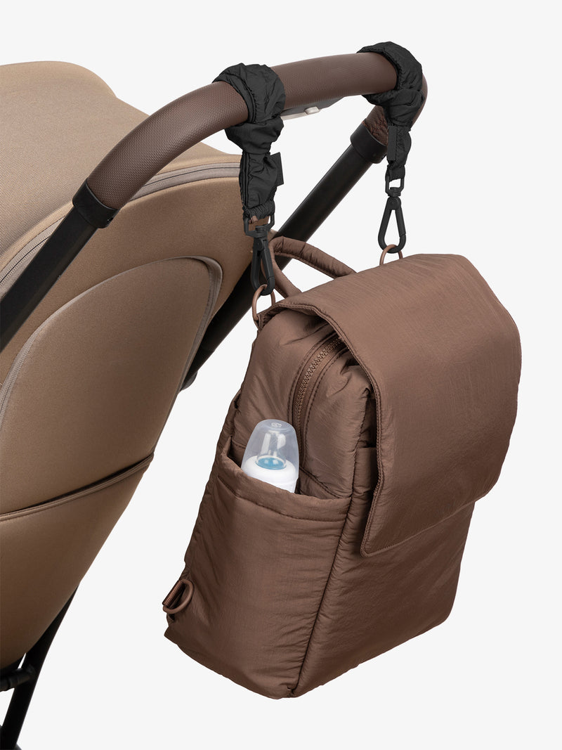 CALPAK Convertible Mini Diaper Backpack in brown Hazelnut with Black Stroller Straps attached to a brown stroller