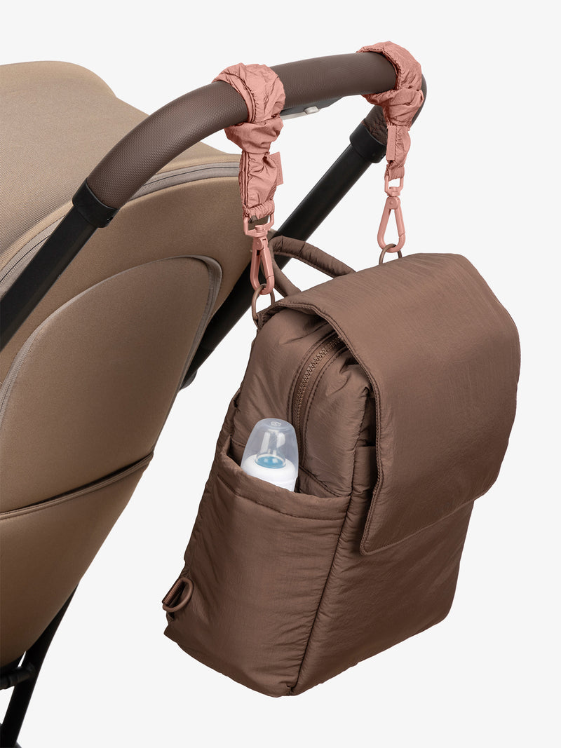 CALPAK Convertible Mini Diaper Backpack in brown Hazelnut with pink Peony Stroller Straps attached to a brown stroller