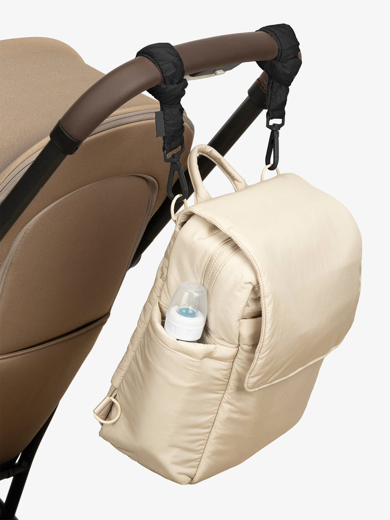 CALPAK Convertible Mini Diaper Backpack in white Oatmeal with Black  Stroller Straps attached to a brown stroller