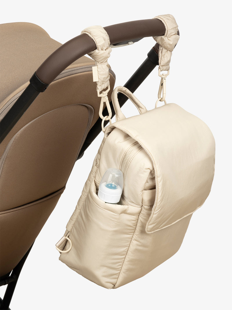 CALPAK Convertible Mini Diaper Backpack in white Oatmeal with white Oatmeal Stroller Straps attached to a brown stroller