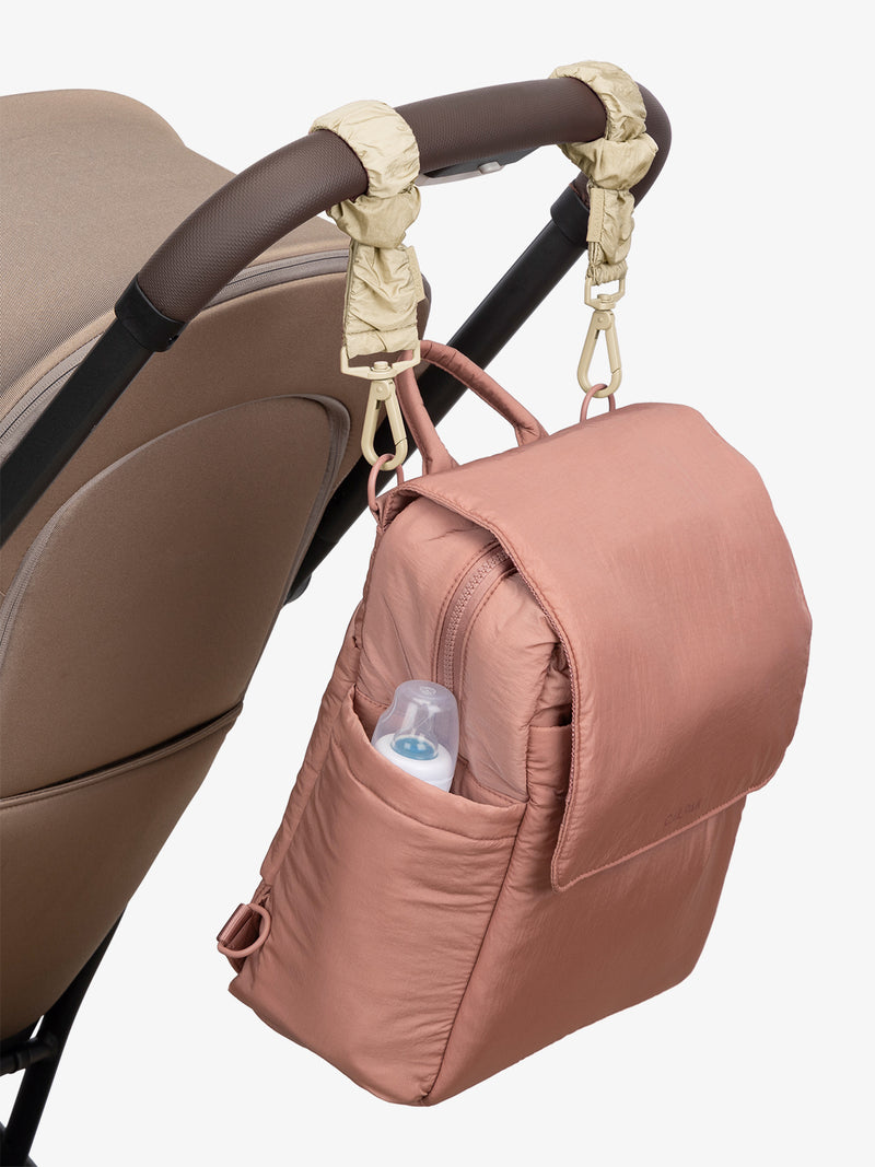 CALPAK Convertible Mini Diaper Backpack in pink Peony with white  Oatmeal Stroller Straps attached to a brown stroller