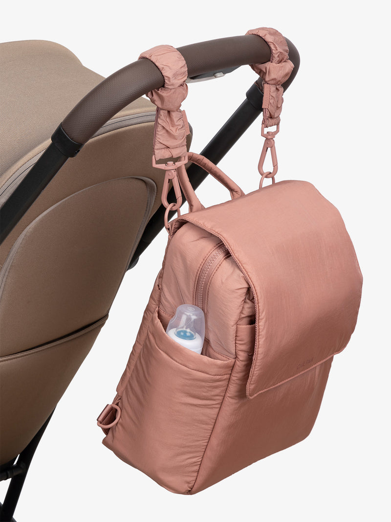 CALPAK Convertible Mini Diaper Backpack in pink Peony with pink Peony Stroller Straps attached to a brown stroller