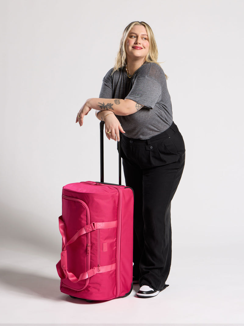 Model standing besides CALPAK Stevyn Large Rolling Duffel in dragonfruit pink