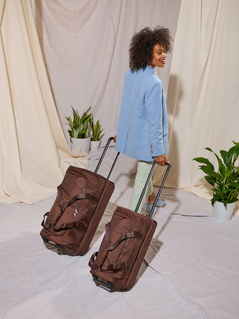 Model rolling CALPAK Stevyn Large Rolling Duffel and Stevyn Rolling Duffel side-by-side for size comparison