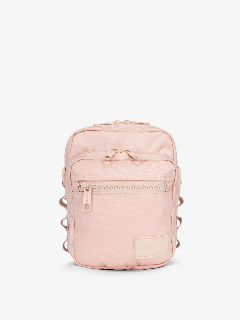 Front-view of CALPAK Stevyn Mini Crossbody Bag with zippered pockets and side panel daisy chains in pink sand