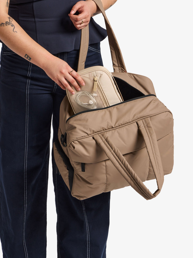 Model placing CALPAK Tech Organizer in beige in CALPAK Luka Duffel