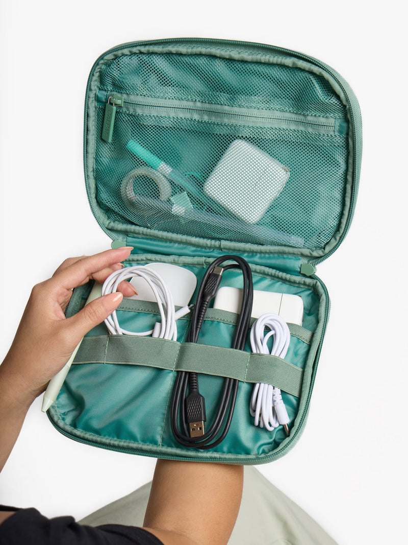 Model displaying electronics organized within interior compartment of the sage green CALPAK tech organizer