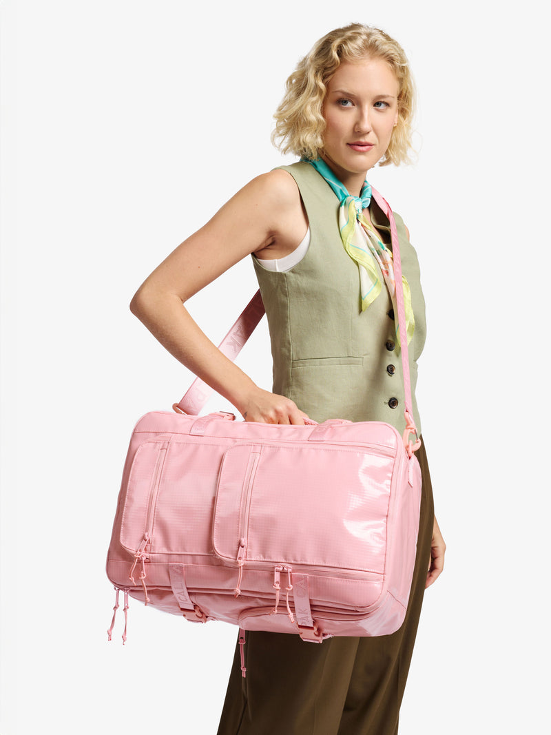 Model wearing CALPAK 26L Laptop Duffel Backpack as crossbody bag with removable crossbody strap included in pink blossom