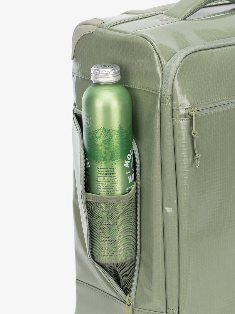 Studio product shot of side bottle holder pocket of CALPAK Terra 35L Carry-On luggage with soft shell and 360 spinner wheels in juniper green