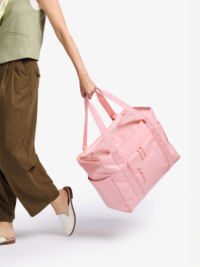 Model holding CALPAK Terra 35L Water Resistant Zippered Tote Bag by durable carrying handles in blossom pink