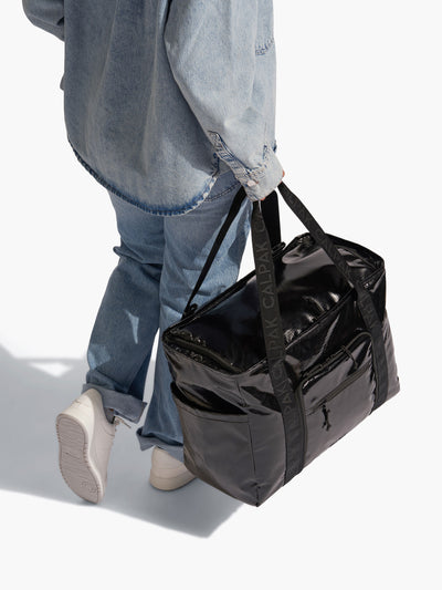 Model holding CALPAK Terra 35L Water Resistant Zippered Tote Bag by durable nylon strap in black