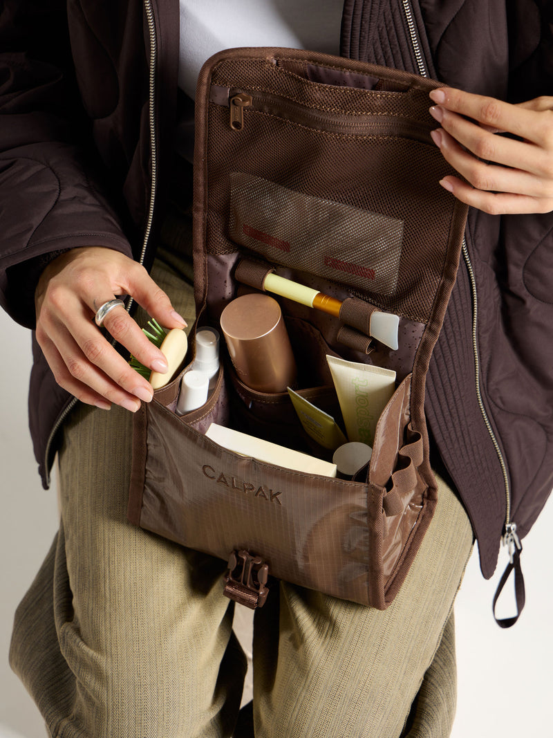 Model displaying interior of CALPAK Terra Hanging Toiletry Bag in cacao