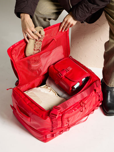 Model placing socks into mesh interior pocket of CALPAK Terra Large 50L Duffel Backpack in red
