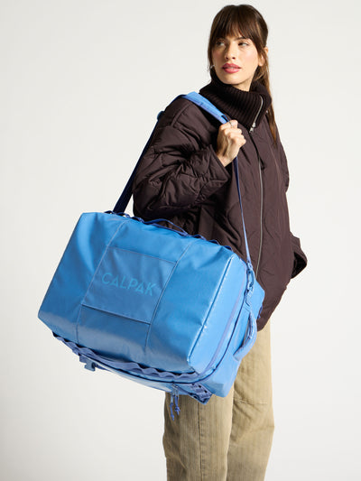 Model wearing crossbody strap of blue CALPAK  terra large 50L duffel backpack over shoulder