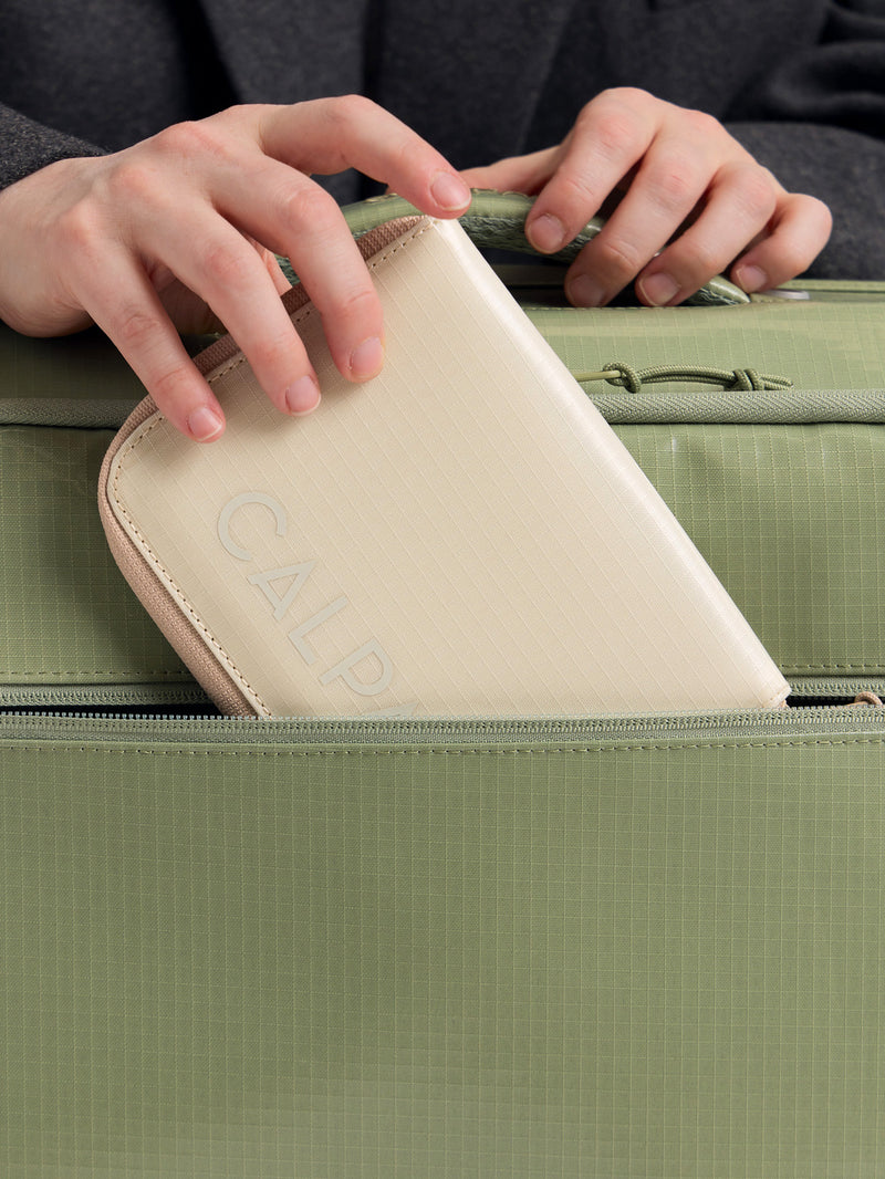 CALPAK Terra Zippered Passport Wallet in beige White Sands with passport being placed inside a bag