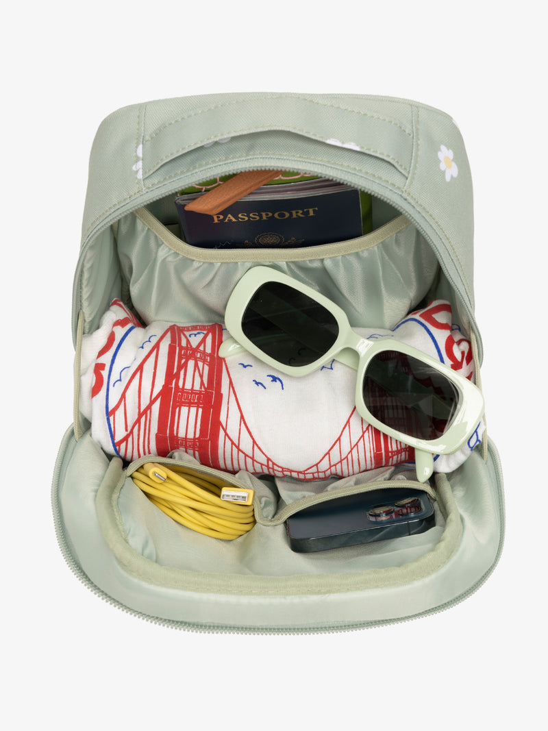 Interior view of daisy CALPAK The Everything Cube with notebook and passport in large slip pocket, cords and phone in front slip pockets, and sunglasses and t-shirt in main compartment