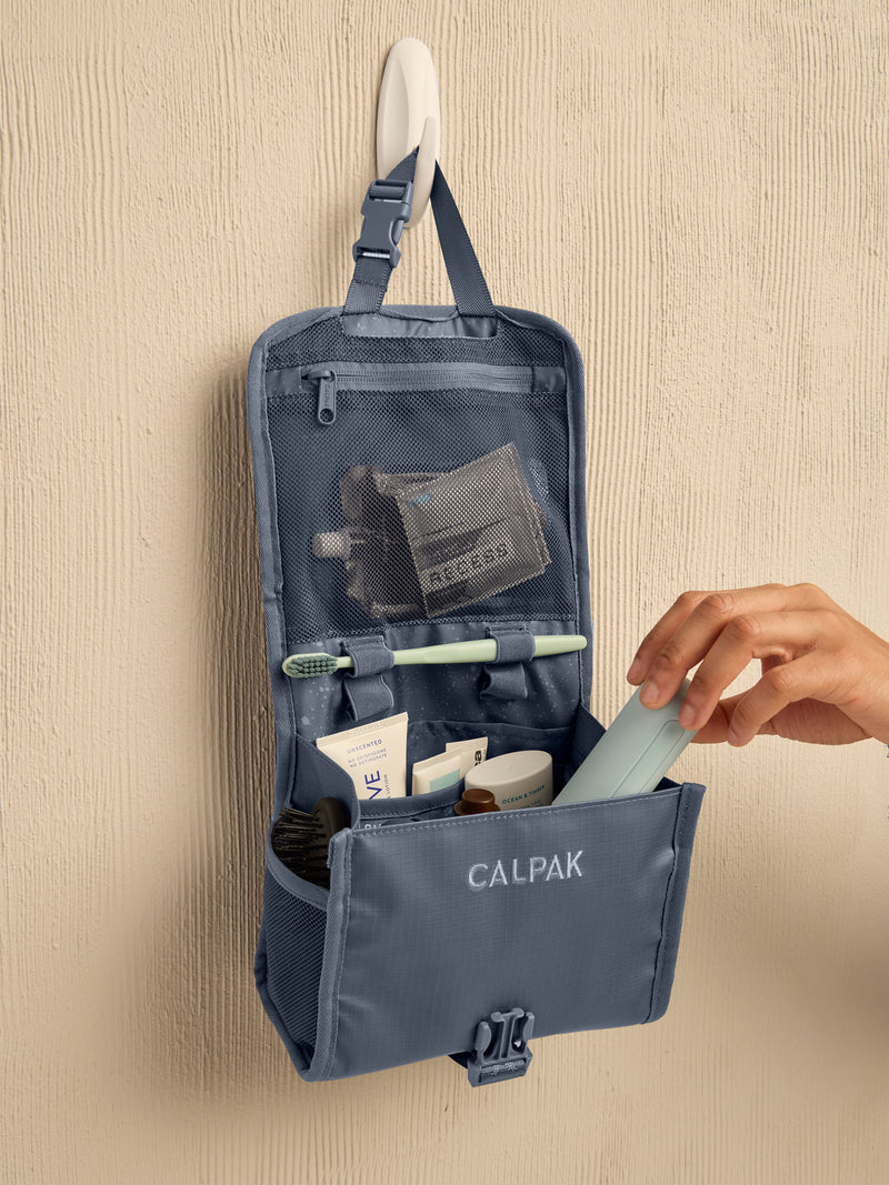 Model adding toiletry items to the CALPAK Terra Hanging Toiletry Bag in blue Matte Indigo