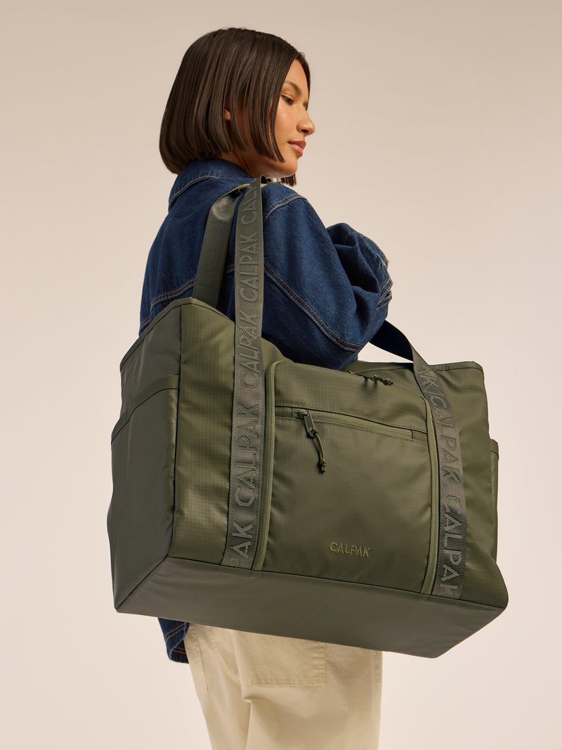 Model wearing the CALPAK Terra 35L Water Resistant Zippered Tote Bag in dark green Matte Pine