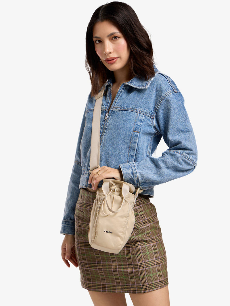 Model wearing beige CALPAK water bottle bag as crossbody bag