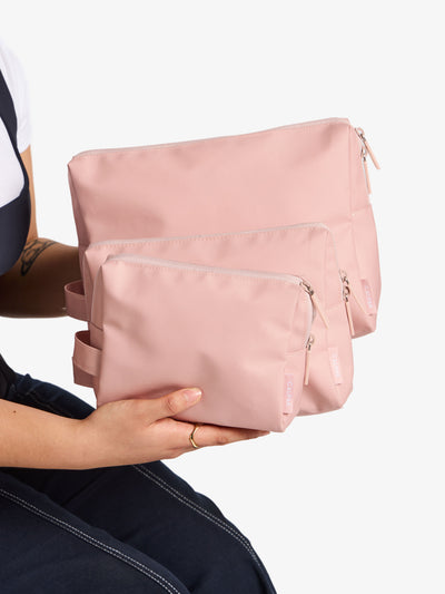 Model displaying the CALPAK waterproof zippered pouch set in small, medium and large in pink