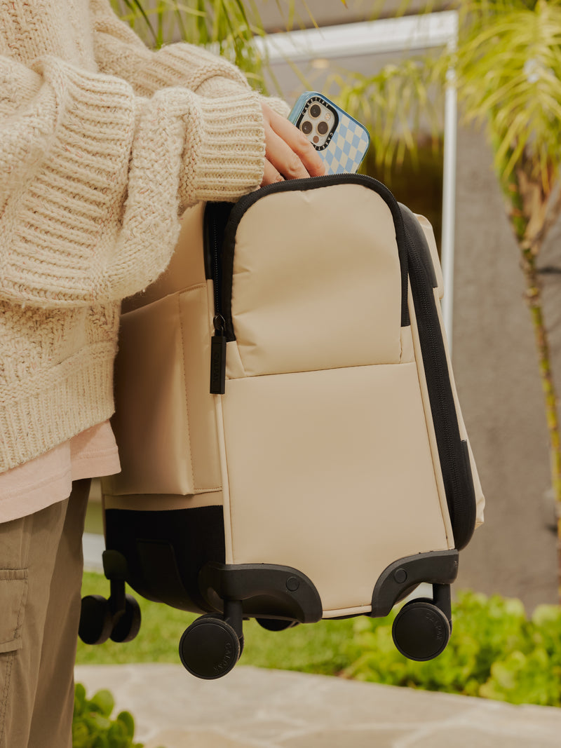 Model carrying CALPAK carry on Luka soft sided luggage with 360 spinner wheels and side pocket in ivory