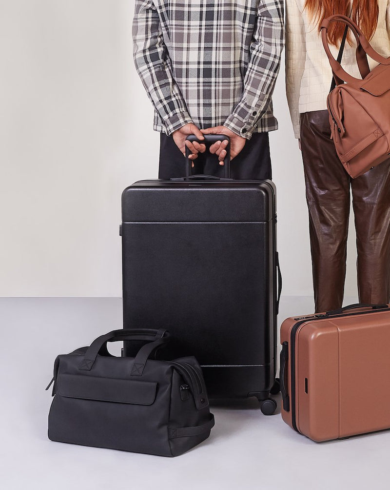 couple with large 30 inch hard shell spinner luggage in black color and other pieces from CALPAK Hue collection